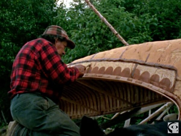 Native gentleman carving designs in the side of the birch bark canoe he is making.