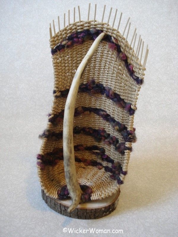 "Primal Trappings" antler basket sculpture by Cathryn Peters made with a red deer antler spike, Danish cord, knubby multi-colored yarn on an ash live-edge base.