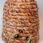 Rustic, straw, coiled bee skep with two little artificial bees at opening, woven by Cathryn Peters.